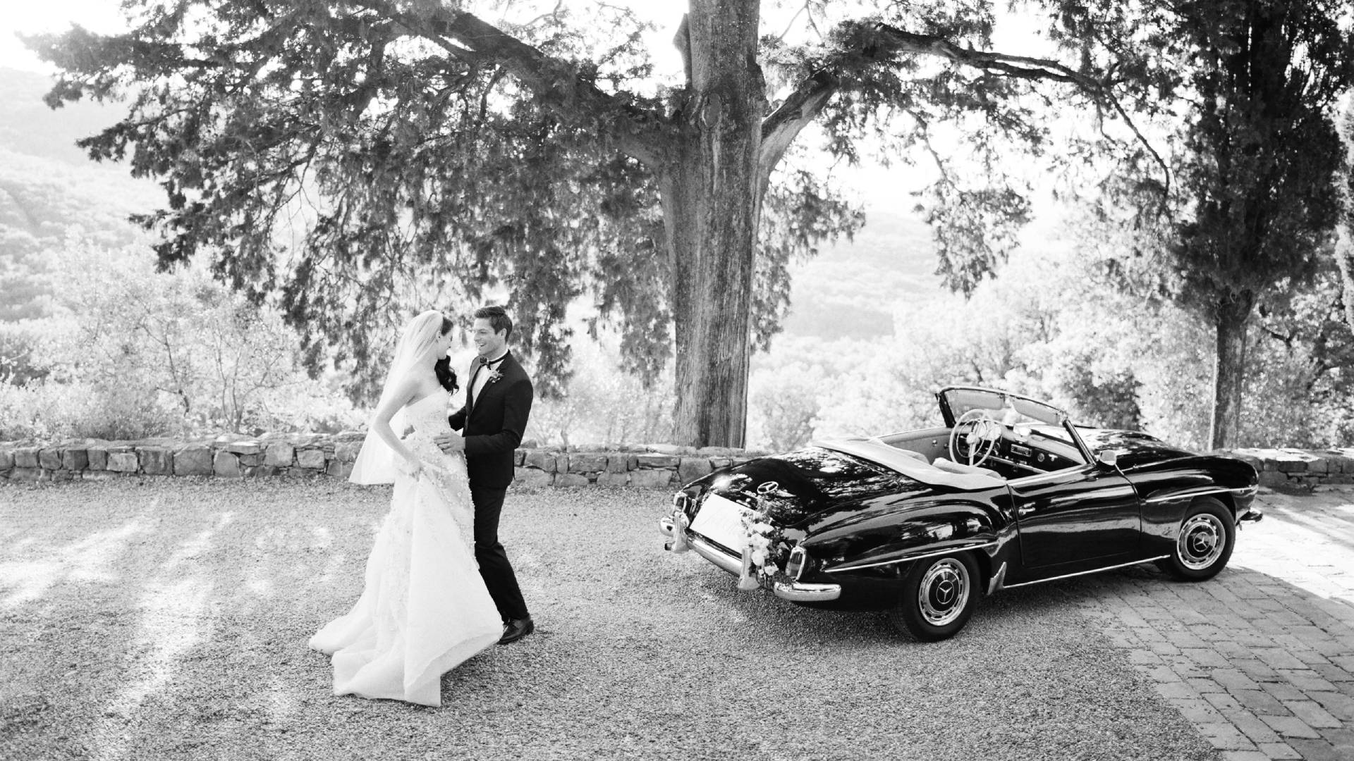 A bride and groom kissing in front of an old car.