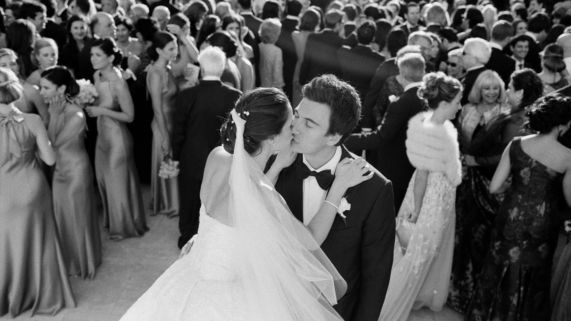 A bride and groom kissing in front of a crowd.